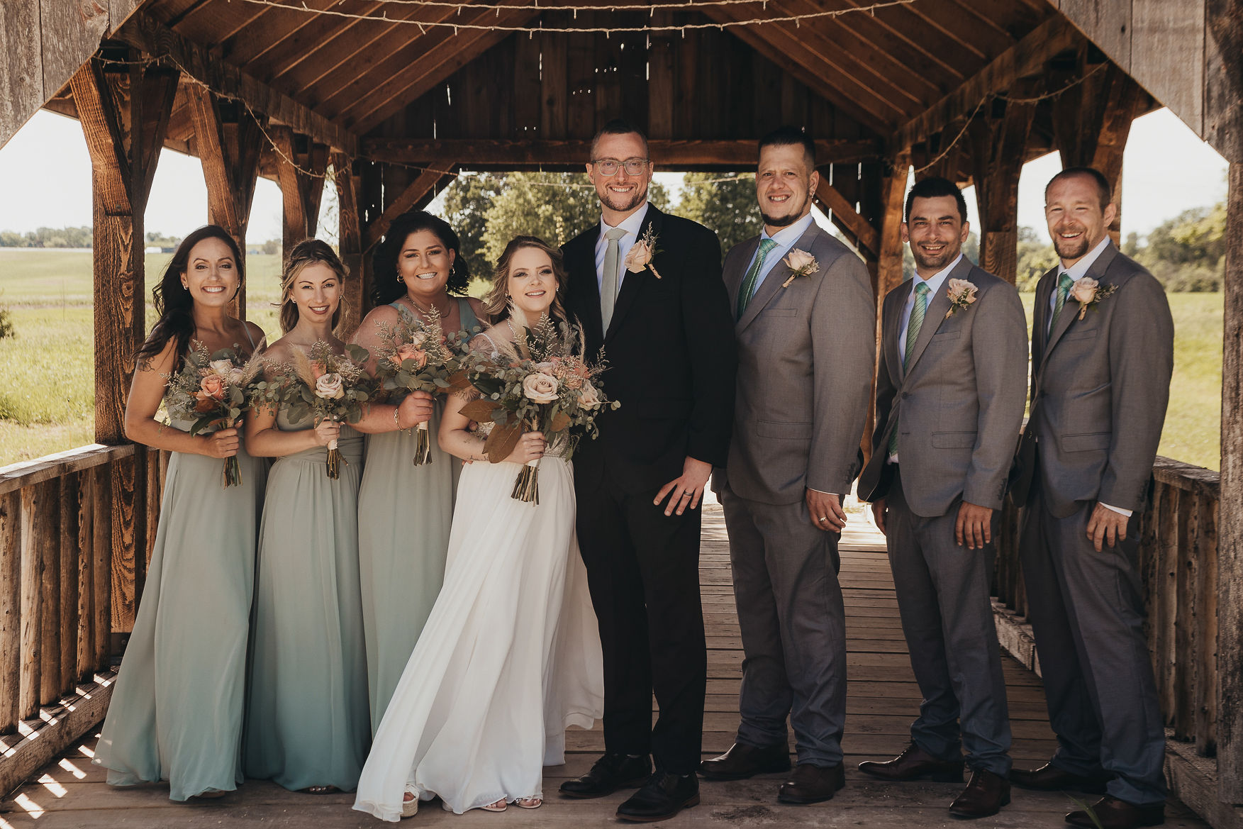 Wedding party in sage green and gray on the wooden covered bridge at Covered Bridge Estate wedding and event venue